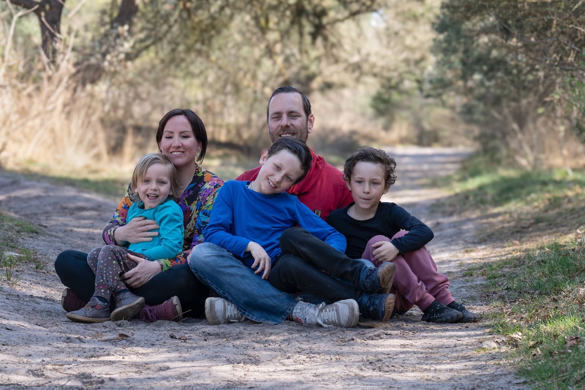 Spontane gezinsfoto met vader, moeder en kinderen die ongedwongen in de natuur zitten.