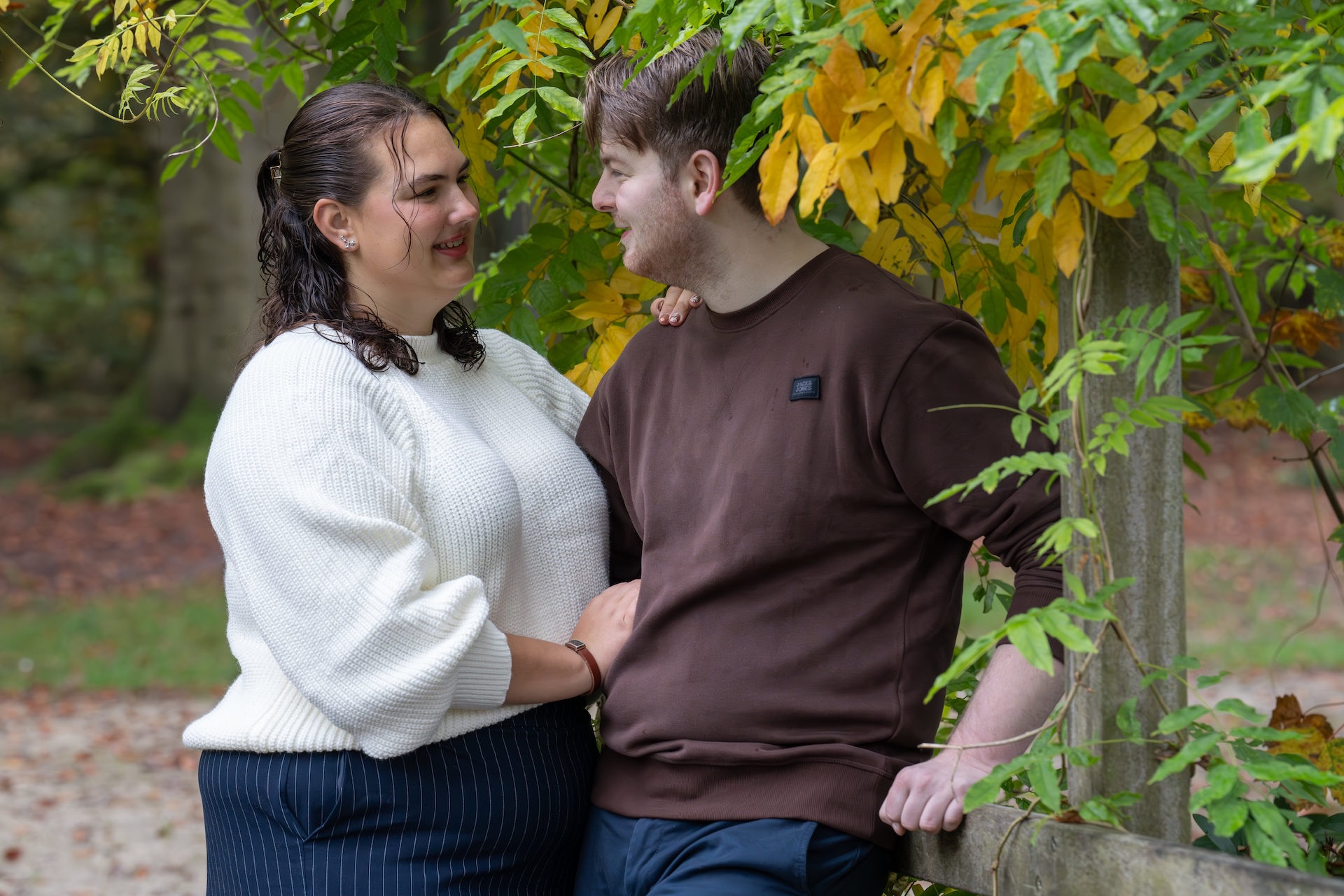 Op een mooie herfstdag twee geliefden samen in het bos tijdens een loveshoot. Het duo kijken elkaar met een warme blik aan.