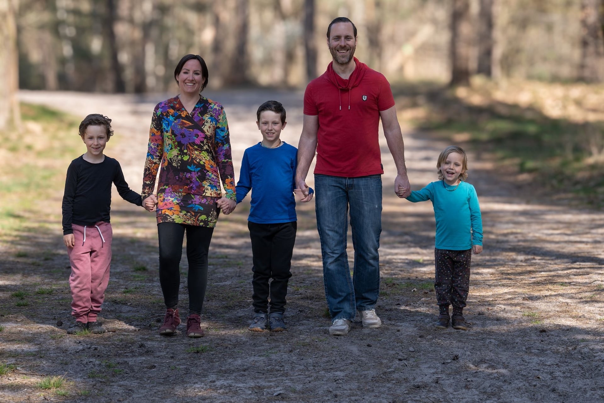 ouders lopen hand in hand met kinderen op een bospad tijdens buiten gezinsfotoshoot.