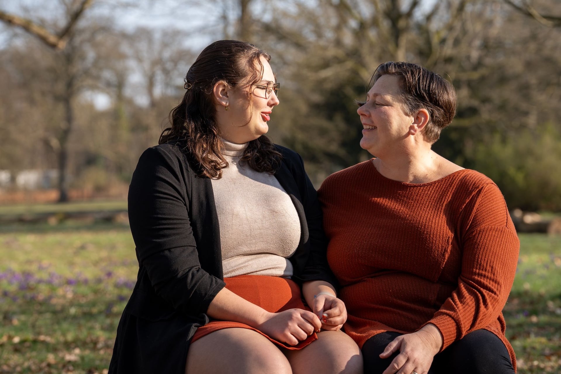 Moeder en dochter zitten op een boomstam in de natuur, hebben aandacht voor elkaar.