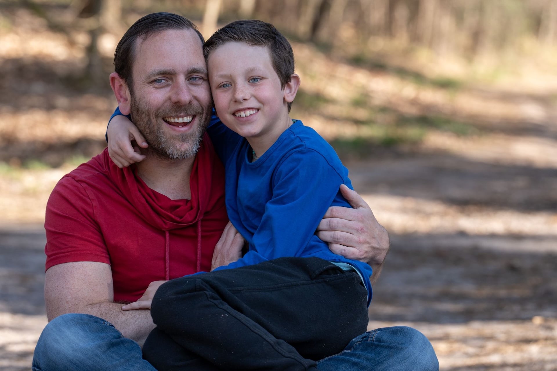 In de natuur zoon bij vader zittend op schoot allebei lachend tijdens een fotosessie met het gezin.
