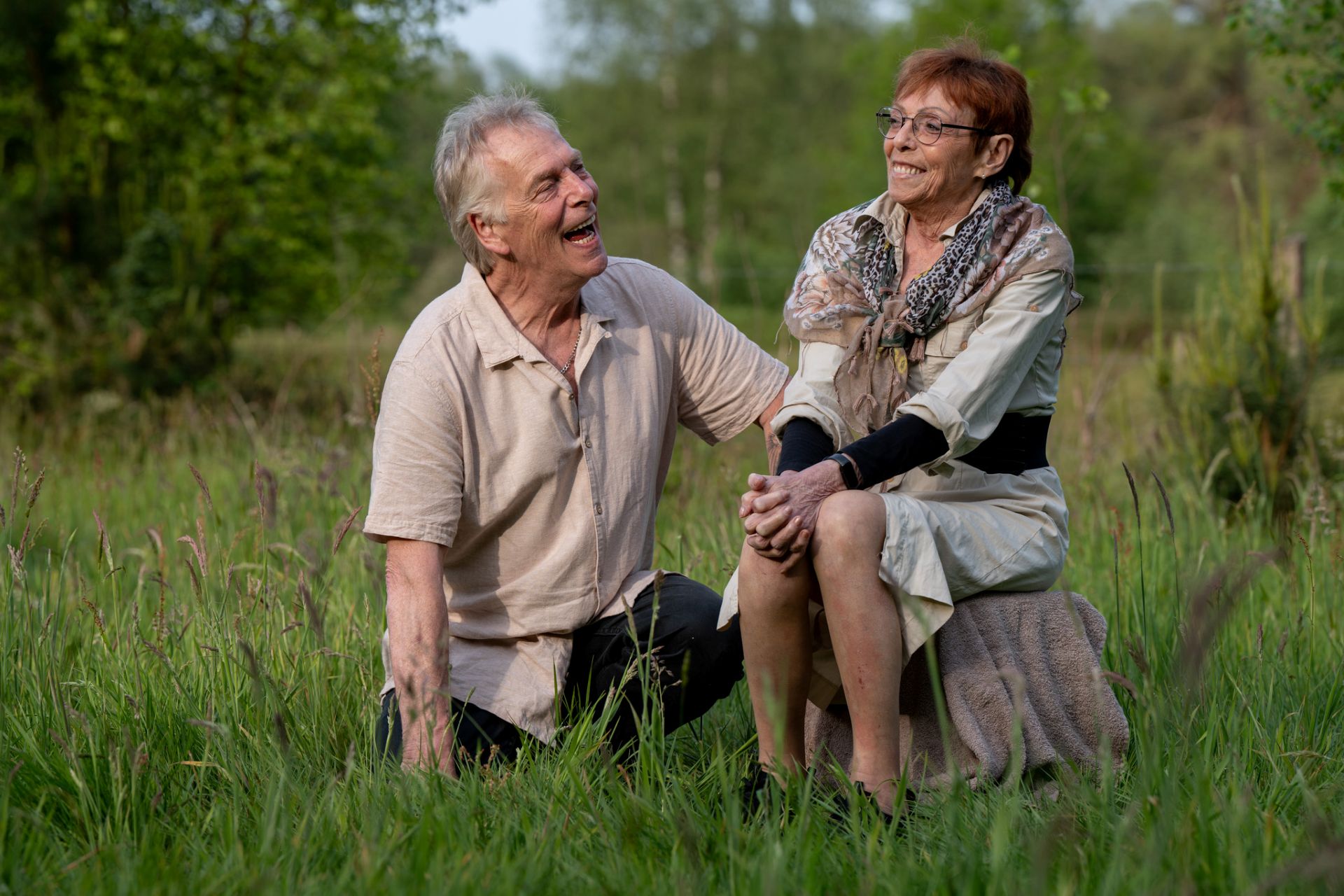 Broer en zus zitten in een grasveld in de natuur omgeving west brabant en kijken oprecht en geintereseerd naar elkaar.